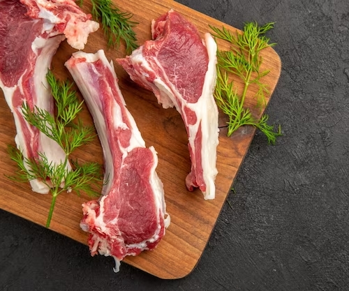 Raw lamb meat on bone on a wood cutting board with herbs around it